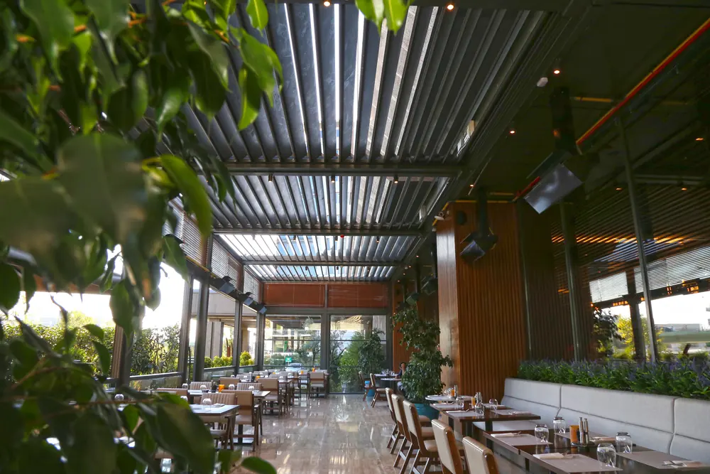 Bioklimatik Pergola: Lamel tavanlı, bitkilerle çevrili restoran salonu