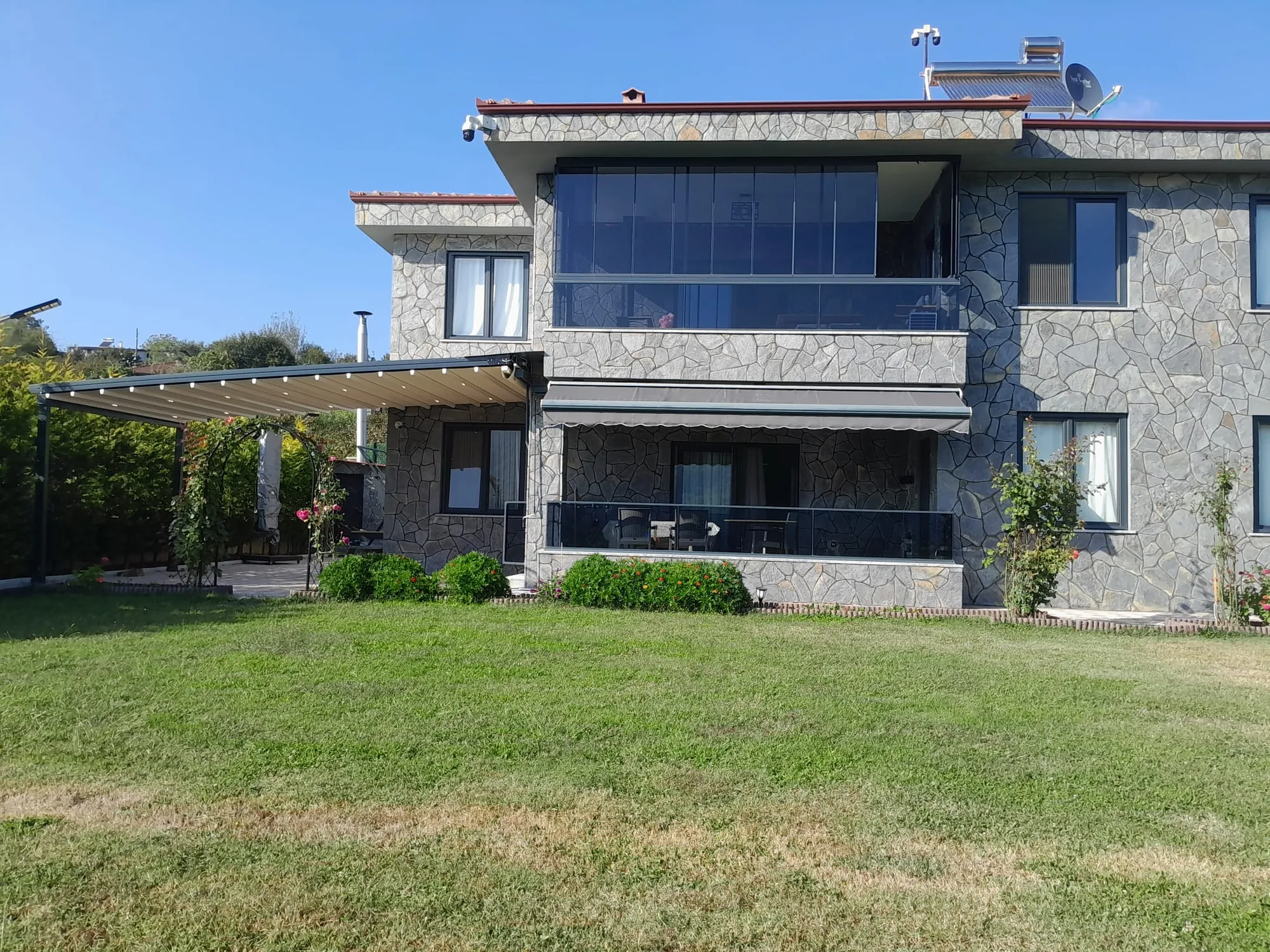 Taş cepheli evde cam balkon ve bahçe pergolası